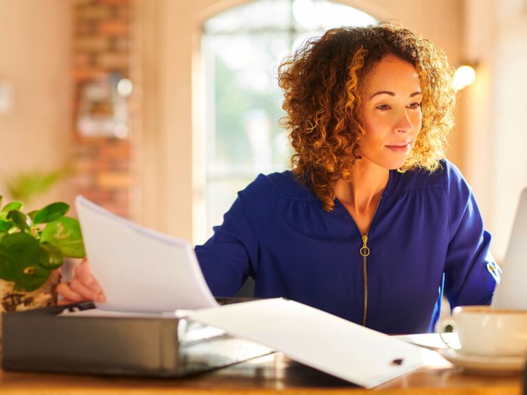 A lady wearing a dark blue blouse sat at her desk working on her laptop.